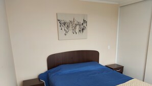 Un dormitorio con cama, mesita de noche, cajón y una obra de arte colgada en la pared.