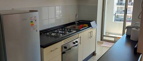 A modern kitchen with a refrigerator, stove, oven, and microwave. There is a window providing a view of the outside.