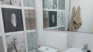 Un baño con inodoro, lavamanos y cortina de ducha con diseño inspirado en la naturaleza.