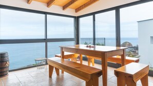 A spacious room with large windows overlooking the sea, wooden furniture, and a tiled floor. - Villa das Escaleiras (Porto Moniz)