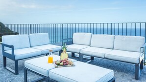 A balcony with a white sofa and a table set with fruits and a drink. - Villa das Escaleiras (Porto Moniz)
