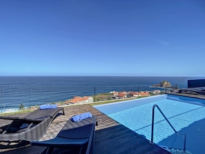 Un área junto a la piscina con sillones de descanso y vista al océano.