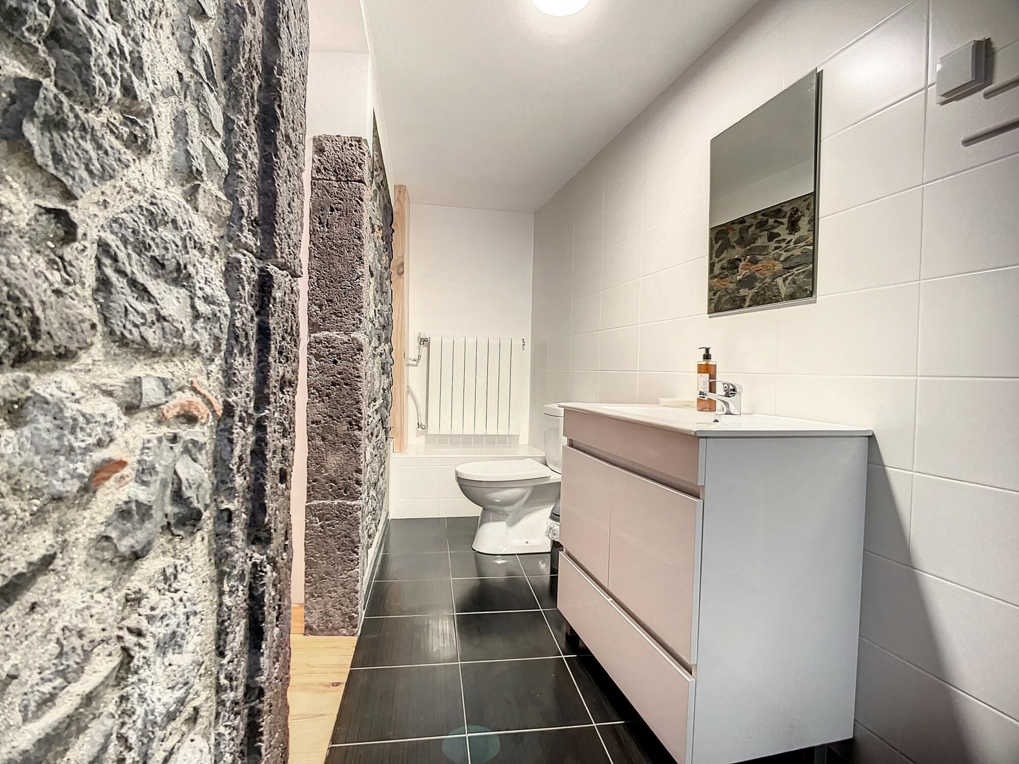 A bathroom with a stone wall, a white toilet, a sink with a mirror, and a tiled floor.