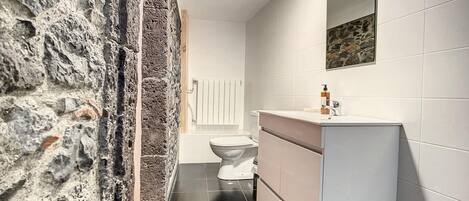 A bathroom with a stone wall, a white toilet, a sink with a mirror, and a tiled floor.