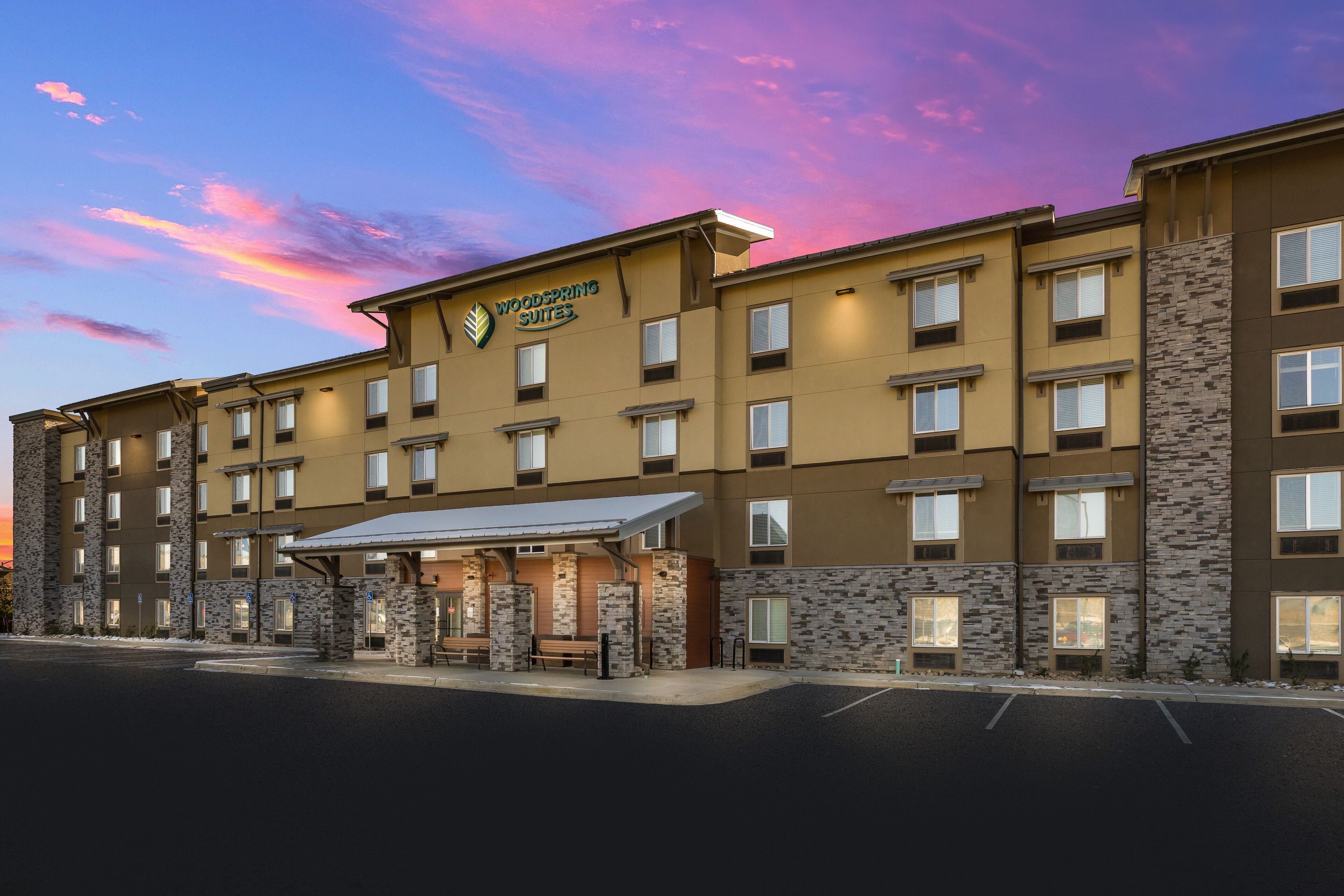 A multi-story hotel with a stone facade, a covered entrance, and a sign reading "Woodspring Suites."