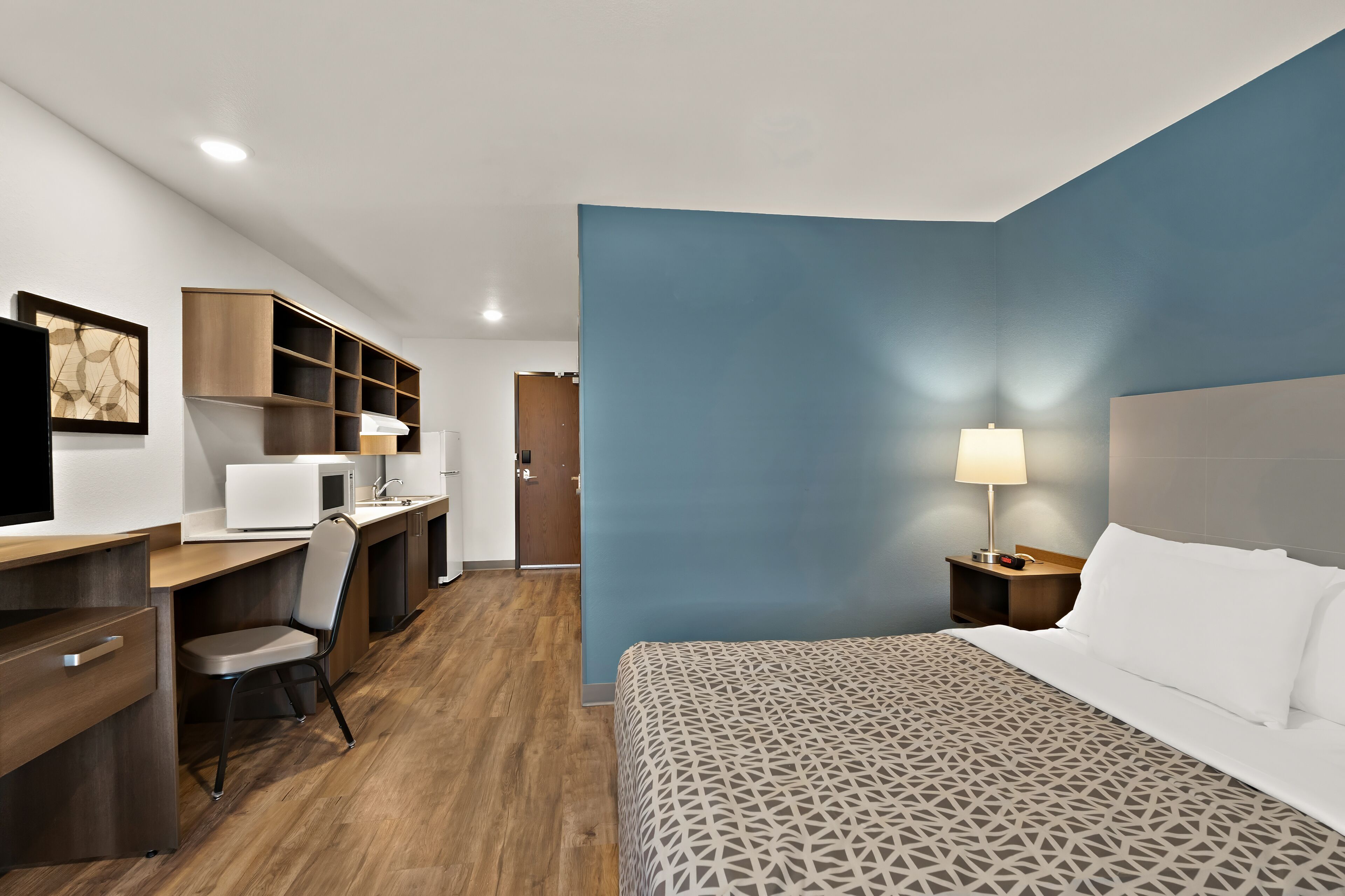 A hotel room with a bed, desk, chair, and a computer.