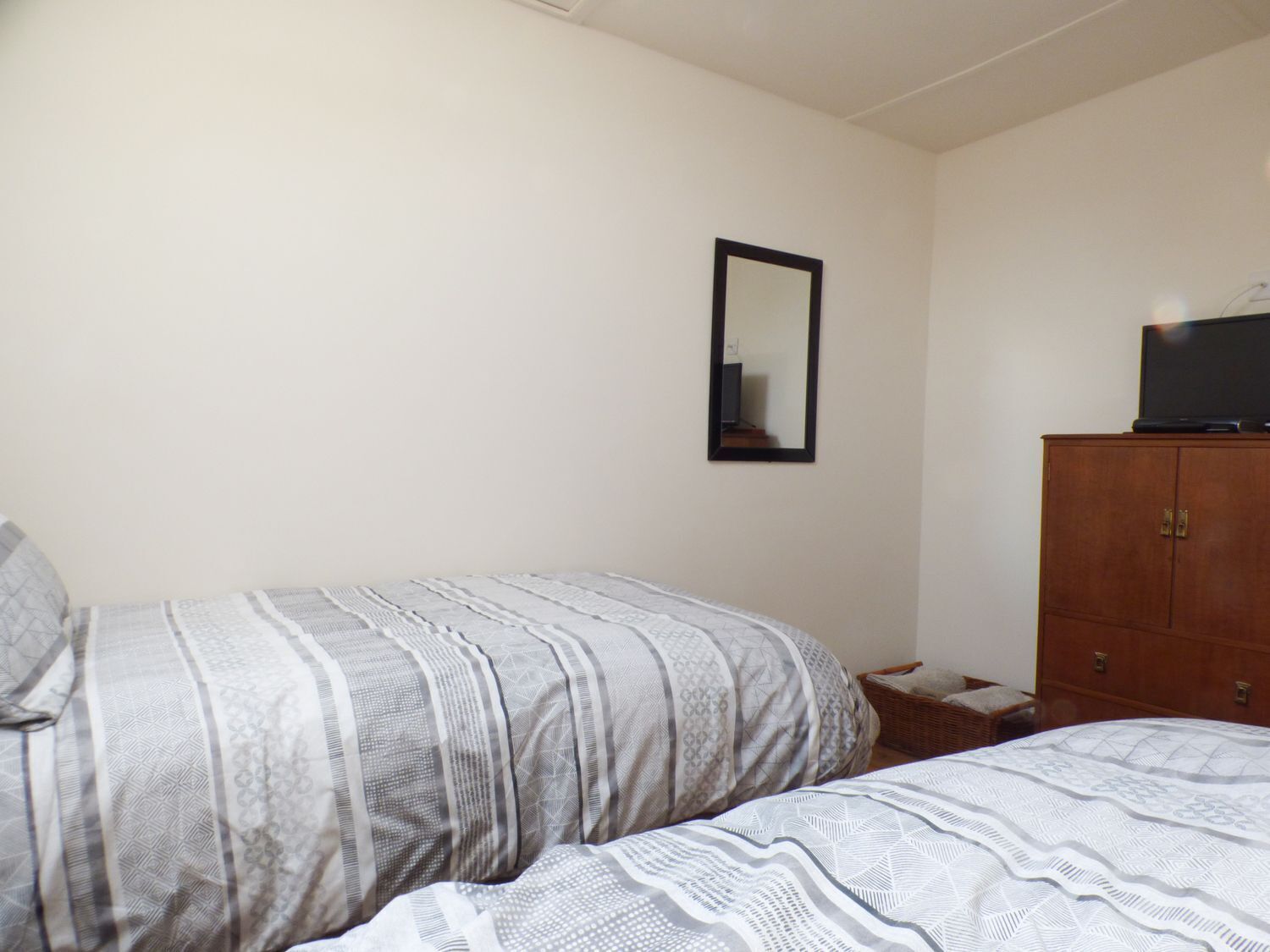 Une chambre avec deux lits, une armoire en bois, un téléviseur posé sur le dessus et un miroir au mur.