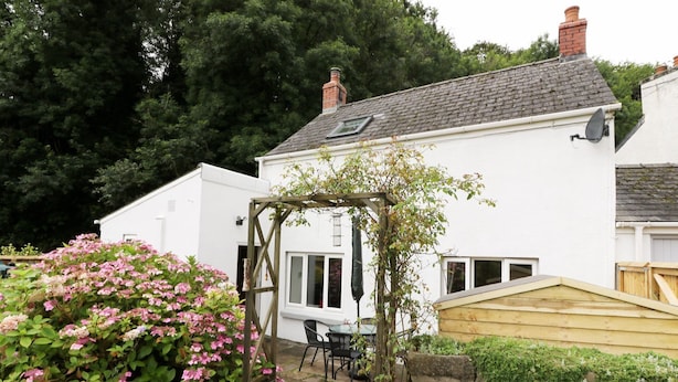 A white house with a stone wall garden, a wooden pergola, and a stone bench. - Spring Garden Cottage (Carmarthen)