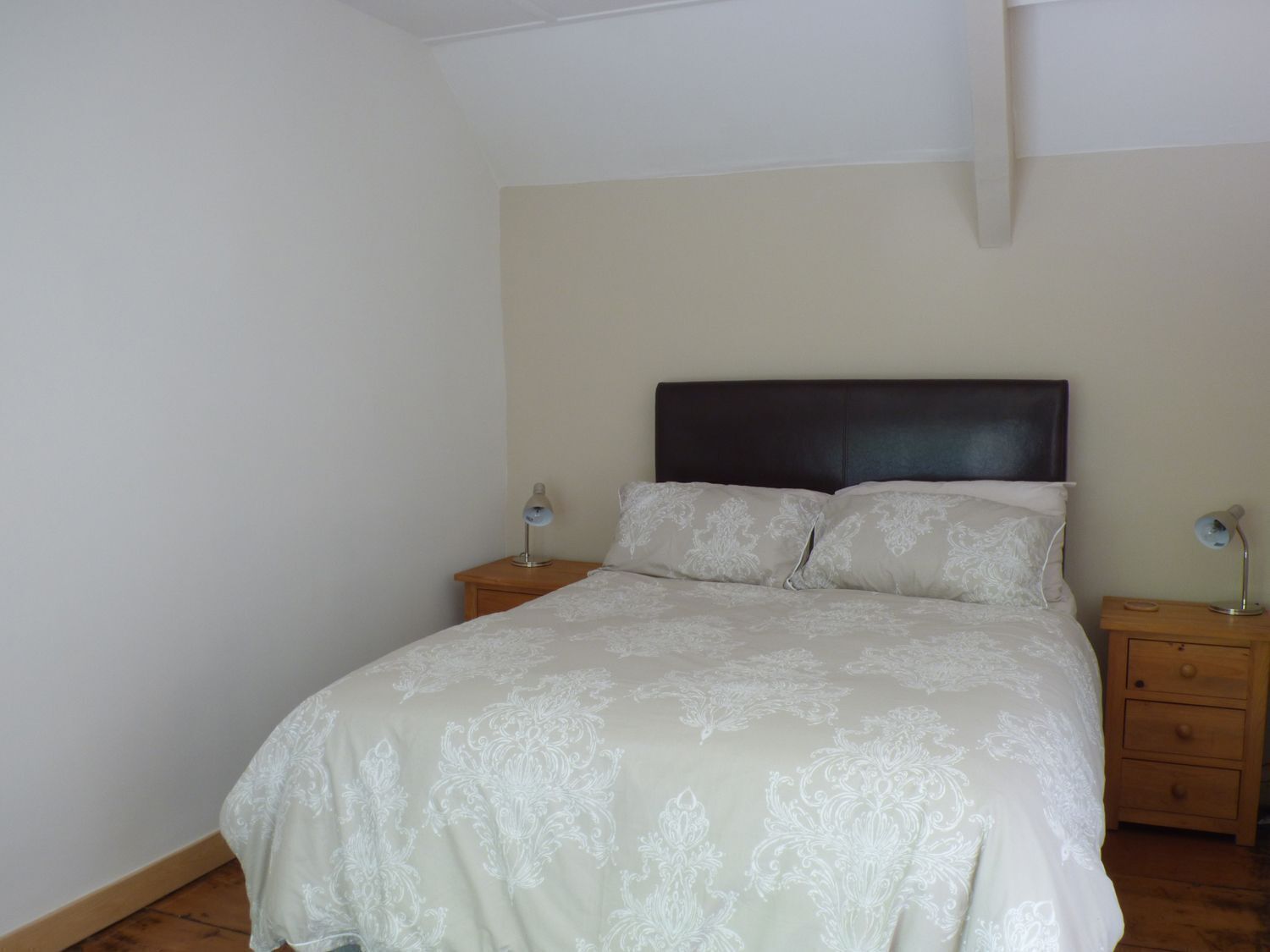 Un dormitorio con cama, dos mesitas de noche y suelo de madera.