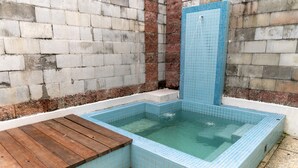 Una bañera de hidromasaje rectangular con mosaicos azules, rodeada por un muro de ladrillo y una terraza de madera.