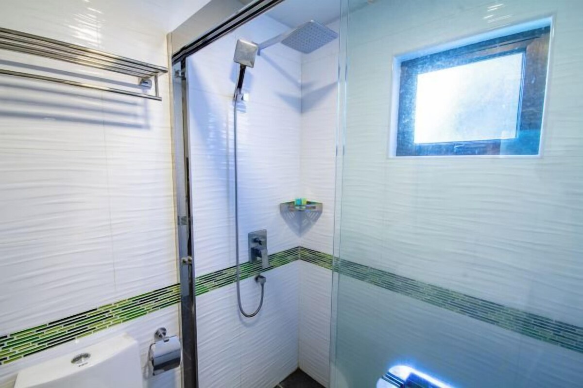 A bathroom with a glass shower enclosure, a toilet, and a small window.