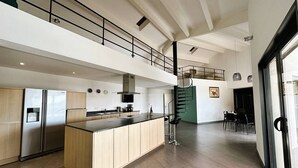 A modern kitchen with a central island, a staircase leading to an upper level, and a dining area with chairs.