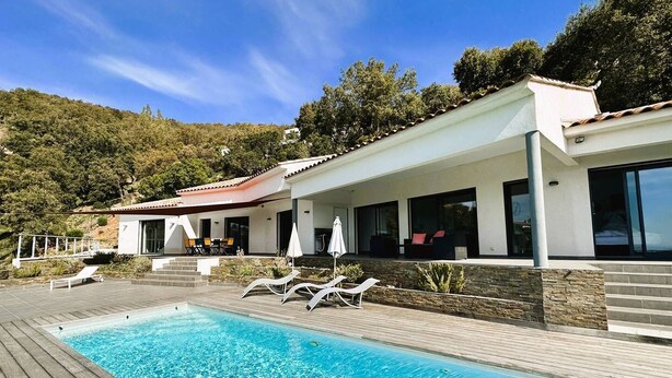 A modern poolside area with a clear blue pool, lounge chairs, and a building with large windows and a covered patio.
