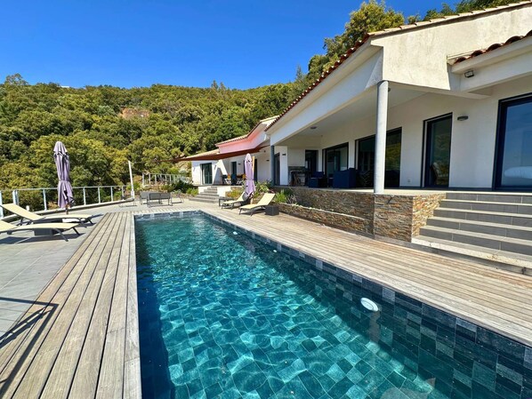 A swimming pool with a wooden deck, lounge chairs, and umbrellas.