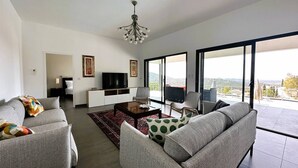 A modern living room with a flat-screen TV, grey sofas, a coffee table, and a chandelier.