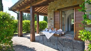 An outdoor patio with stone flooring, wooden pergola, and a table set for dining.