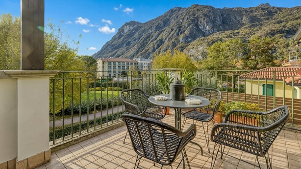 A balcony with wicker furniture, a table, and a view of mountains. - Porto Letizia Orchidea 6, Porlezza, Italy (Porlezza)