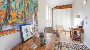 A modern living room with a large abstract painting, a wooden coffee table, a chair, and a TV stand with a basket. - Porto Letizia Orchidea 6, Porlezza, Italy (Porlezza)