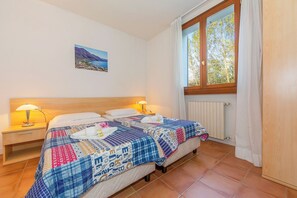 Quarto com duas camas, uma mesa de cabeceira com luminária, uma janela com cortinas e um quadro fixado na parede.