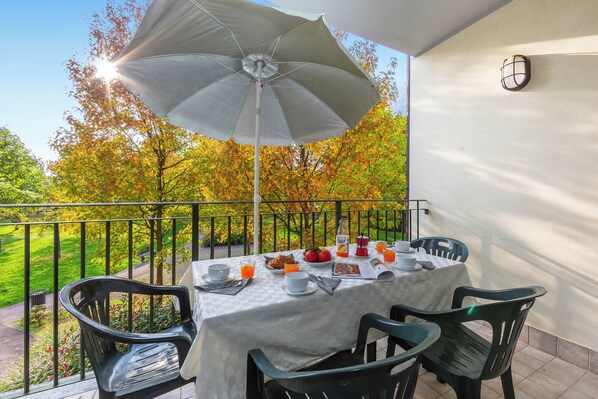 A balcony with a table set for breakfast, outdoor chairs, and a view of trees.