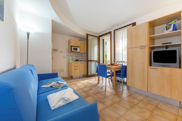 A modern room with a blue sofa, a dining table with chairs, a kitchen area, and a TV. - Porto Letizia Torino 3, Porlezza, Italy (Porlezza)