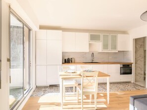 Une cuisine moderne avec des meubles blancs, un plan de travail en bois et un coin repas comprenant une table et des chaises.