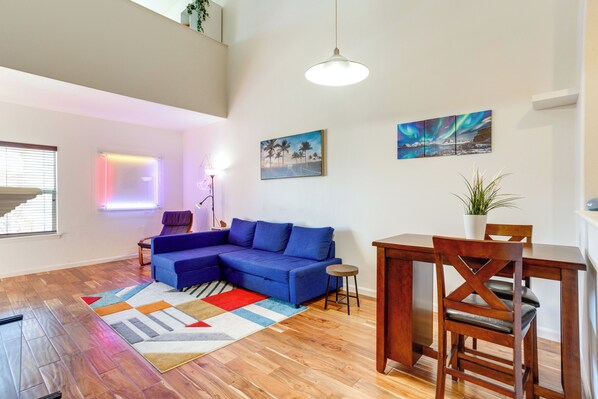 Uma sala de estar moderna com um sofá seccional azul, mesa de jantar de madeira e um tapete colorido.