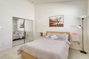 Quarto com cama, espelho, mesa de cabeceira, abajur e um quadro na parede.
