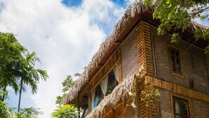 A rustic wooden house with a thatched roof, surrounded by lush greenery and stone steps leading to the entrance. - Puluong Luna Resort (Pu Luong)