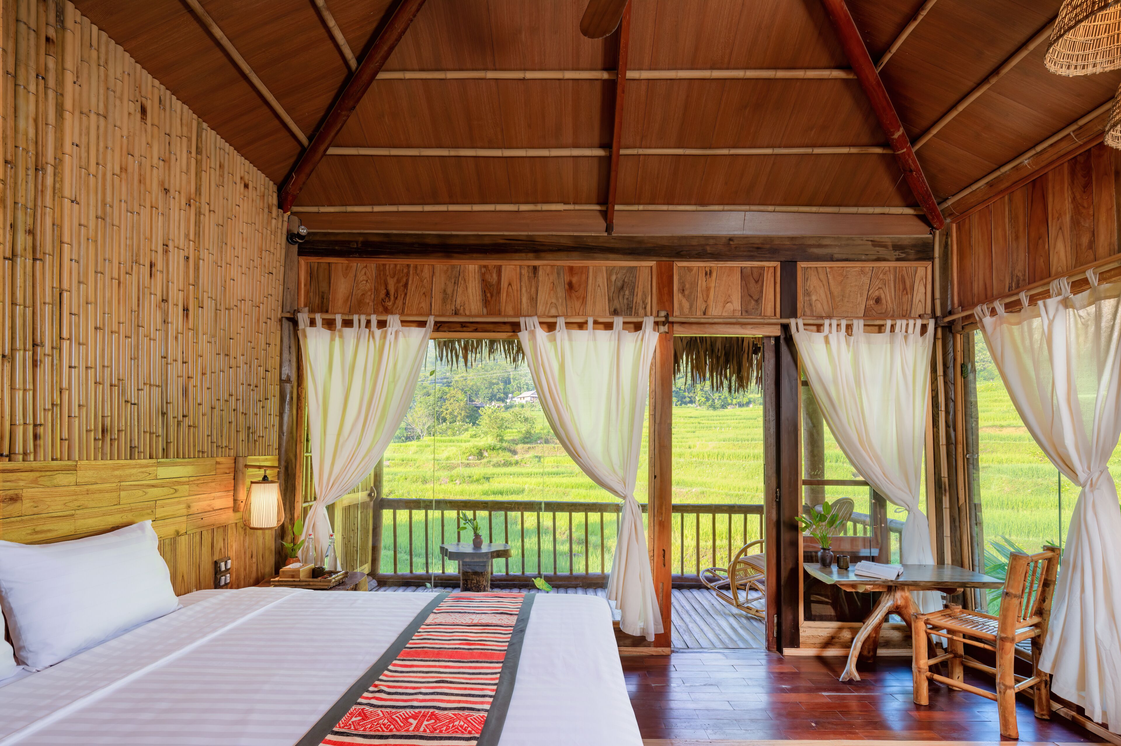 A wooden room with a bed, curtains, and a view of a green landscape.