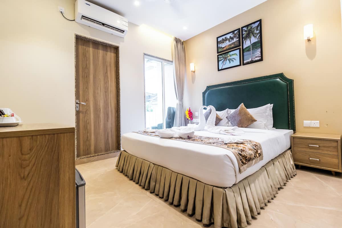 A hotel room with a large bed, a wooden wardrobe, a bedside table, and a window with curtains.