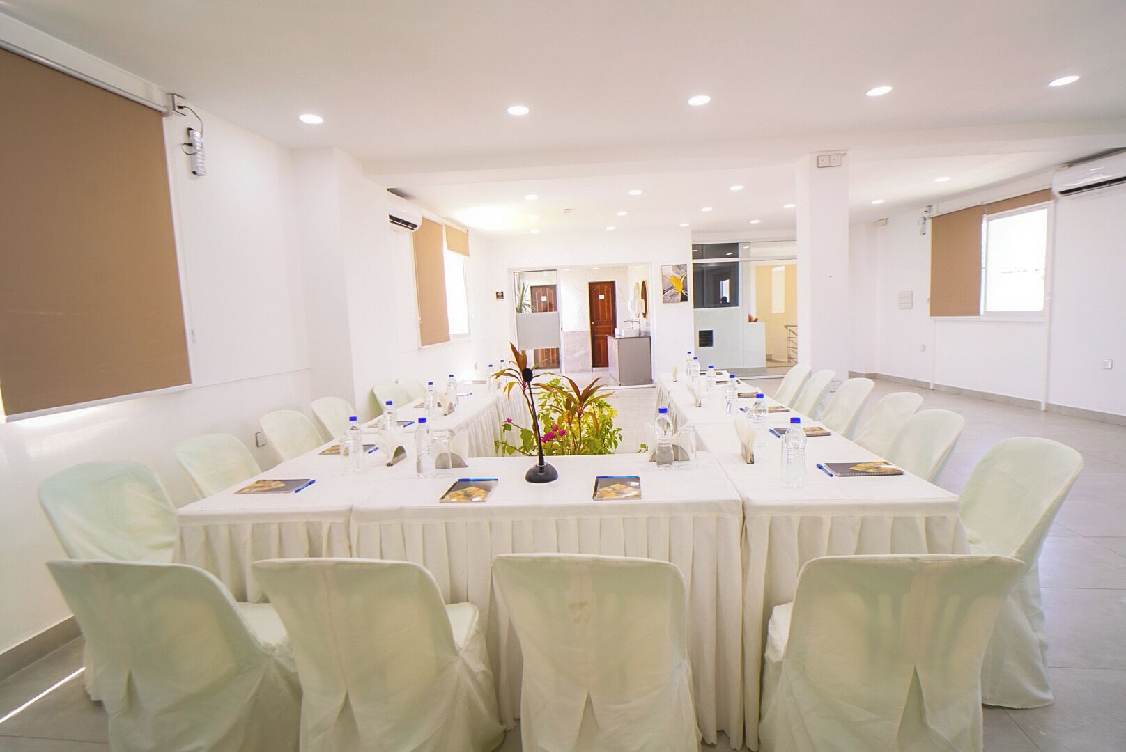 Un salón de conferencias con una larga mesa, sillas y un centro de mesa con planta.