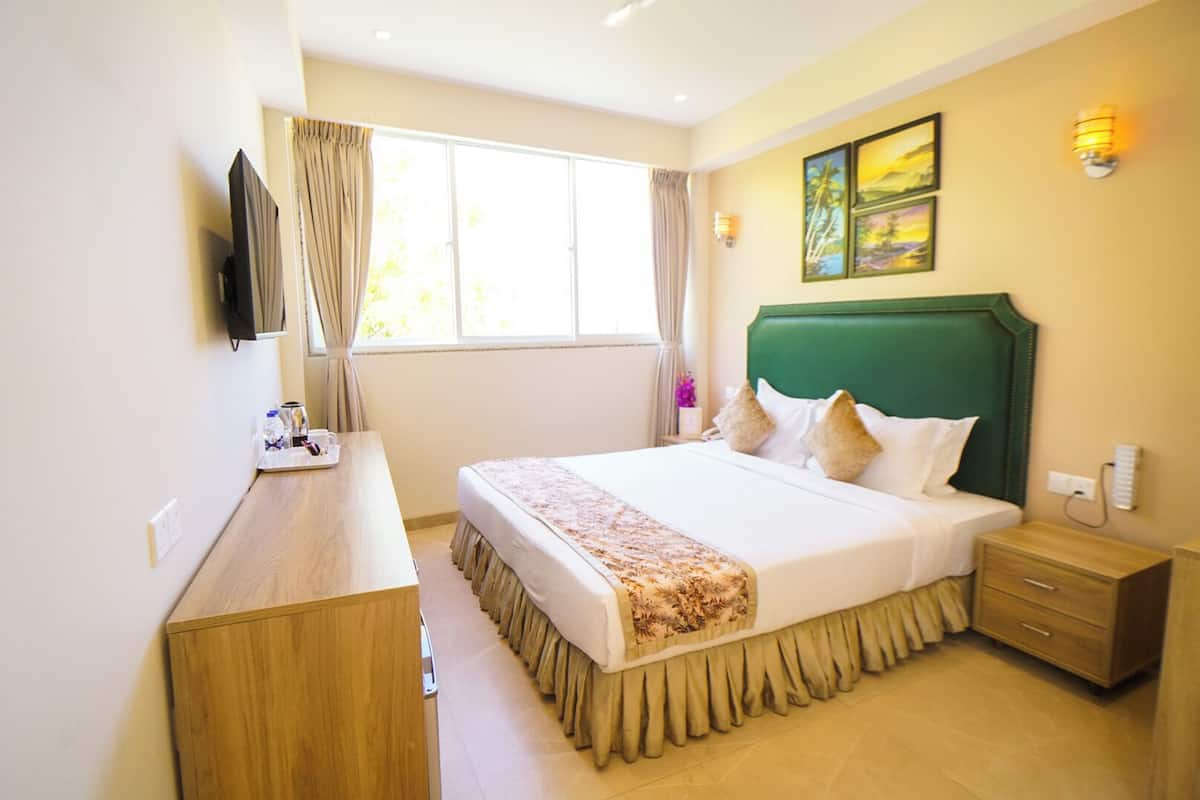 A hotel room with a large bed, a wooden desk, a TV, and a window with curtains.