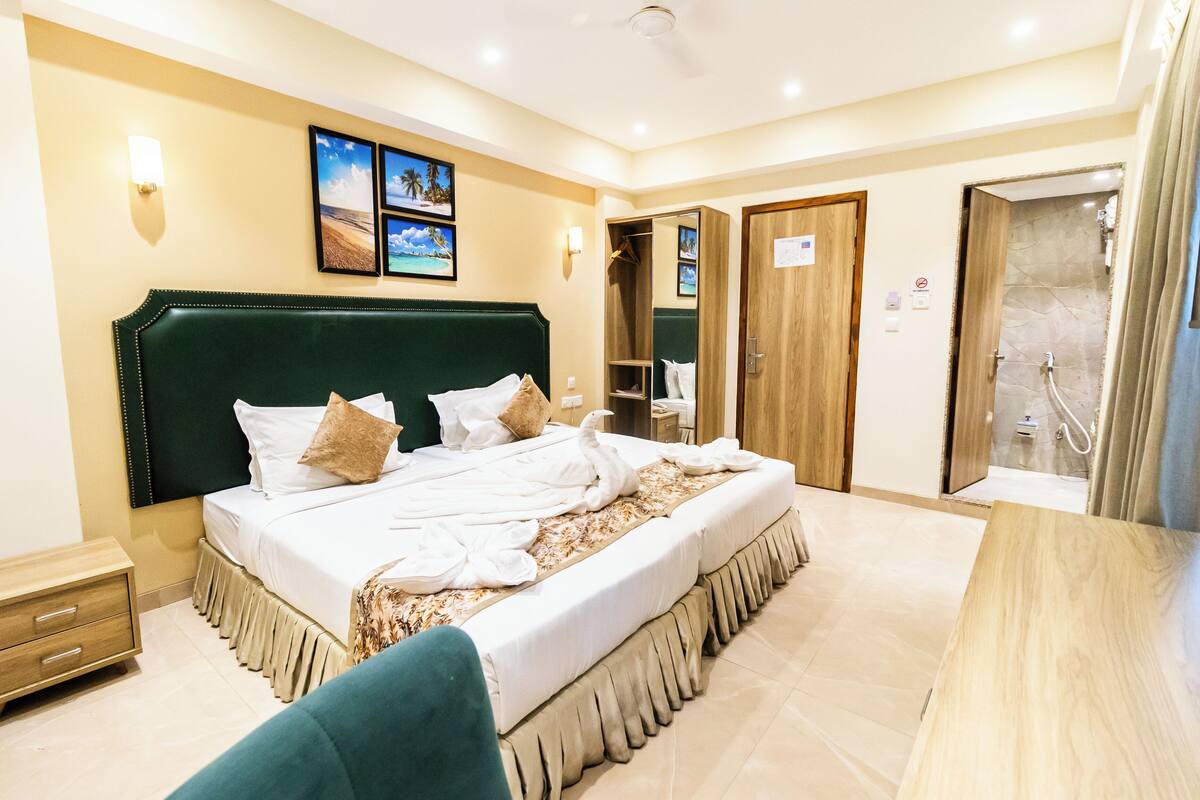 A hotel room with a large bed, a wardrobe, a bathroom with a shower, and a small table.