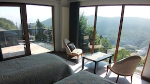 Quarto com duas camas, uma cadeira, uma mesinha e grandes janelas com vista para as montanhas.