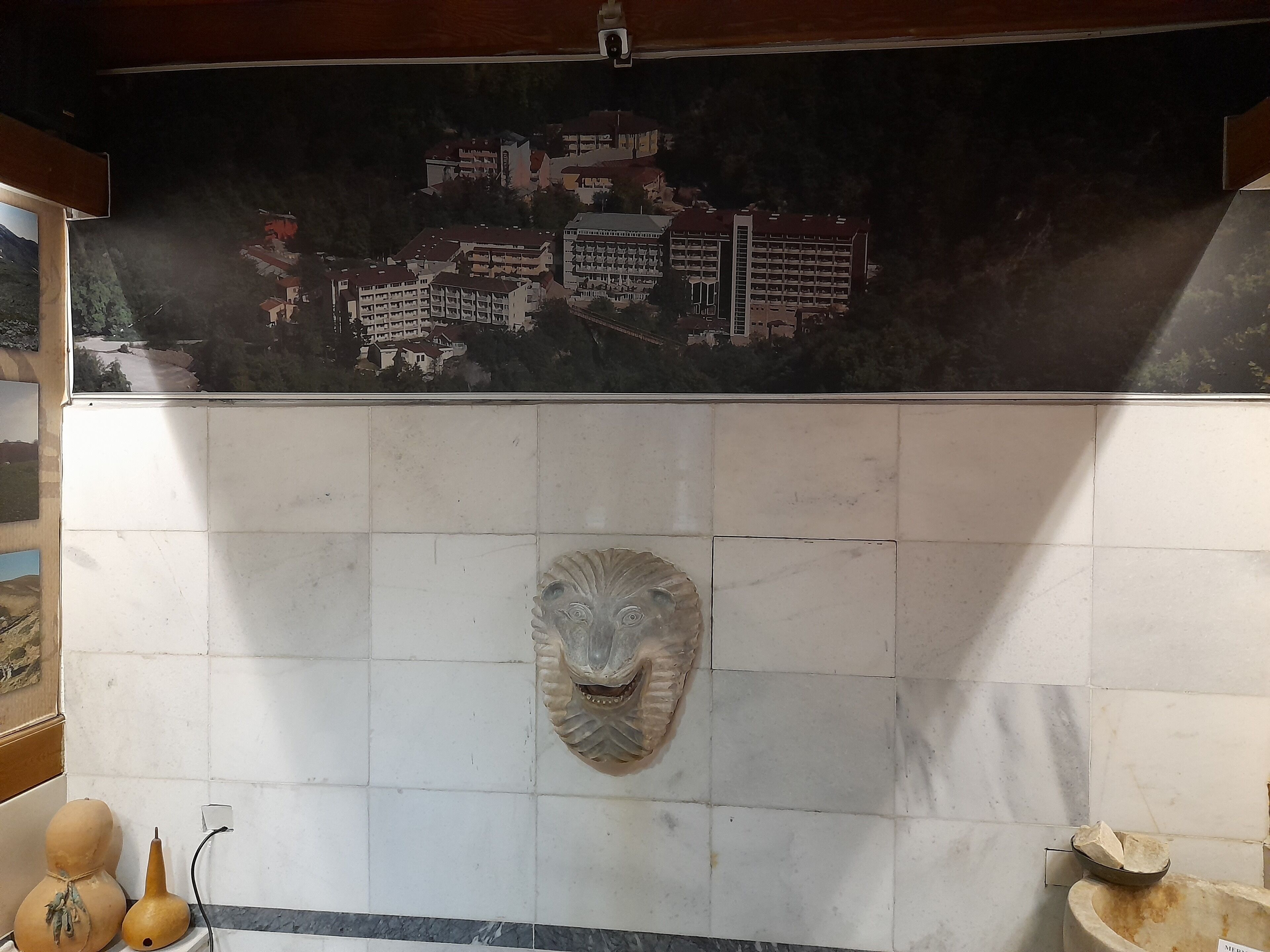 Una pared de azulejos con un mural de paisaje urbano, una máscara de piedra y un cuenco pequeño.