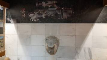 Una pared de azulejos con un mural de paisaje urbano, una máscara de piedra y un cuenco pequeño.