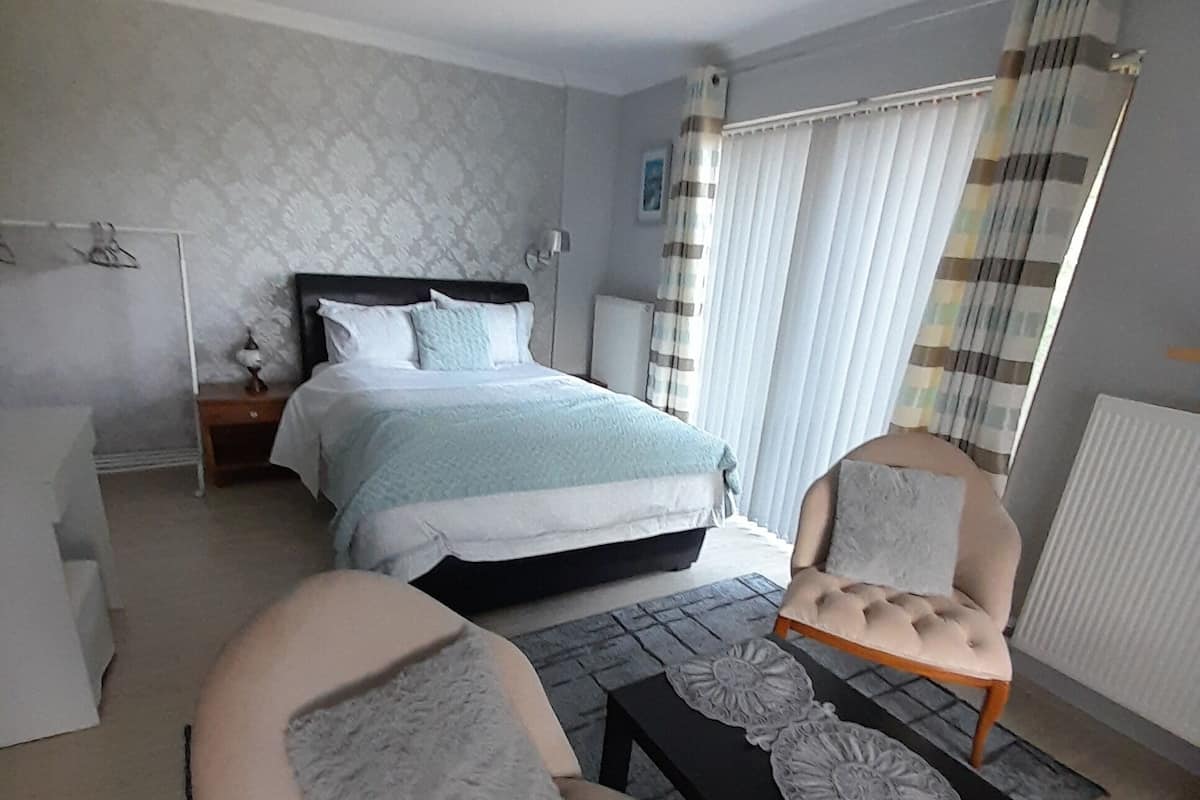 A bedroom with a bed, a chair, a table, and a bedside table.