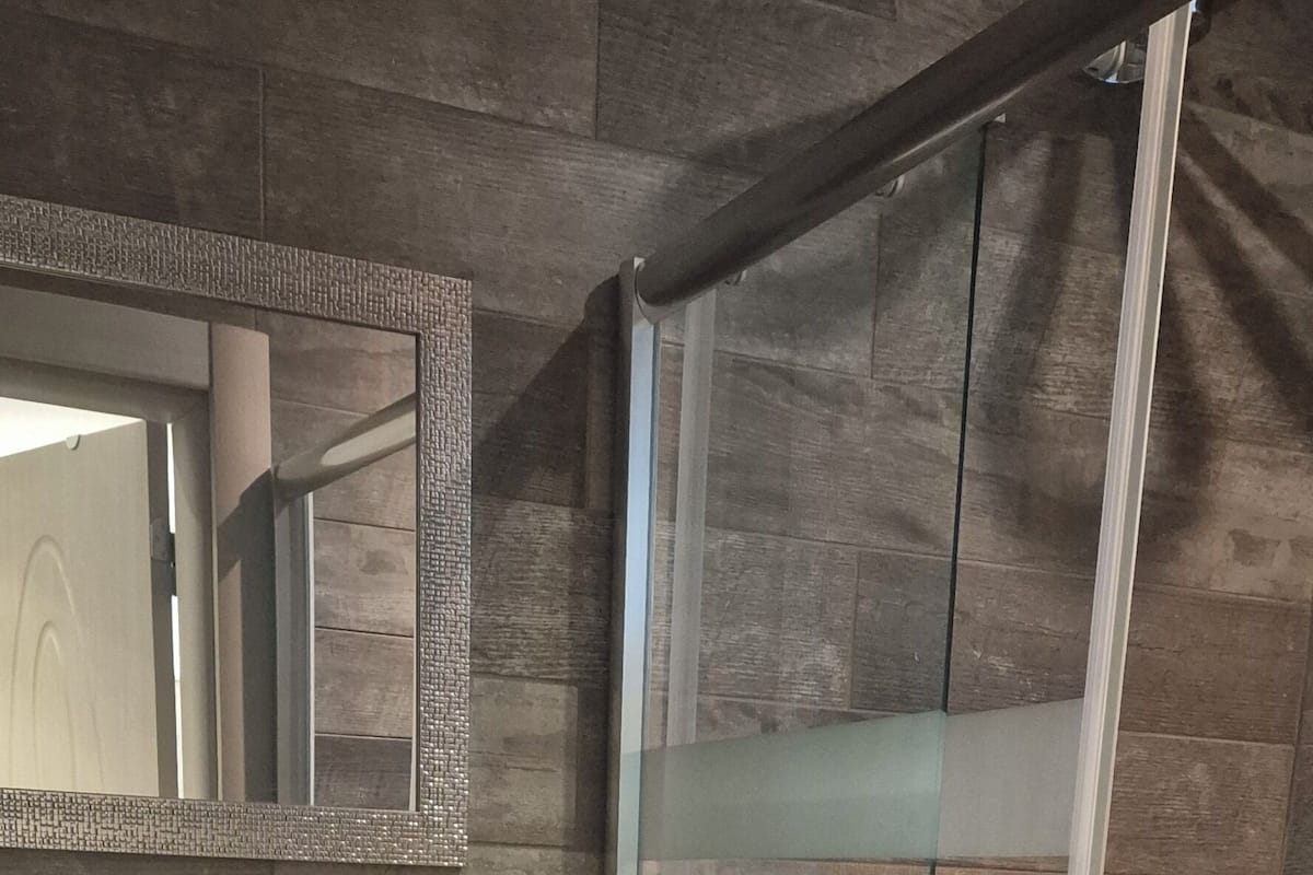 A bathroom with a stone sink, a glass shower enclosure, and a mirror with a decorative frame.