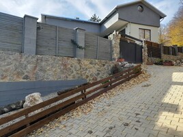 A modern building with a stone wall, a wooden fence, and a paved area with scattered leaves.