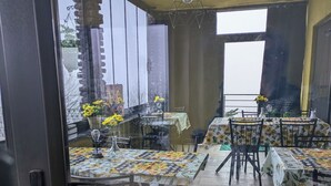 Uma área de refeições em ambiente interno com várias mesas e cadeiras, grandes janelas e um lustre decorativo.