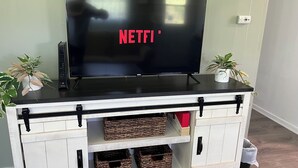 A flat-screen TV on a white cabinet with black handles, two potted plants, and wicker baskets.