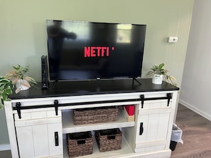 A flat-screen TV on a white cabinet with black handles, two potted plants, and wicker baskets.