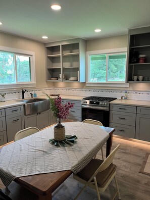 A kitchen with a dining table, chairs, a vase with flowers, and a stove.
