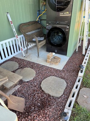 A patio area with a wicker chair, a washing machine, a white picket fence, and a stone pathway.