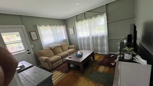 A living room with a sofa, a coffee table, a TV, and a window with sheer curtains.