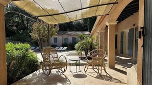 Eine Terrasse im Freien mit Korbmöbeln, Fliesenboden und einer Pergola, die Schatten spendet.