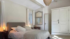 Ein Schlafzimmer mit Bett, Nachttischen, Kommode, Kleiderschrank und einem Fenster mit Vorhängen.
