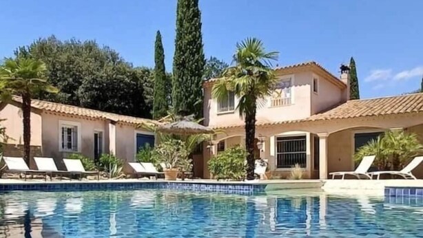 Ein Pool mit gefliesten Rändern, umgeben von Liegestühlen und Palmen, mit Gebäuden im Hintergrund.