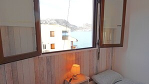 A bedroom with two beds, a nightstand with a lamp, a window with a view of buildings and water, and a mirror on the wall. - Garza Playa - Altea, Costa Blanca (Altea)